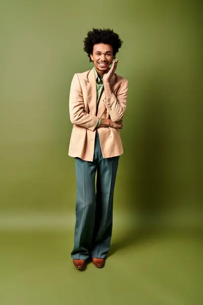 Стильний молодий афроамериканський чоловік у костюмі впевнено стоїть перед яскравим зеленим тлом. — стокове фото