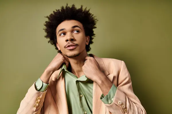 Um jovem afro-americano elegante com cabelo encaracolado, vestindo uma jaqueta de terno e uma camisa verde, posa com confiança contra um fundo verde. — Fotografia de Stock