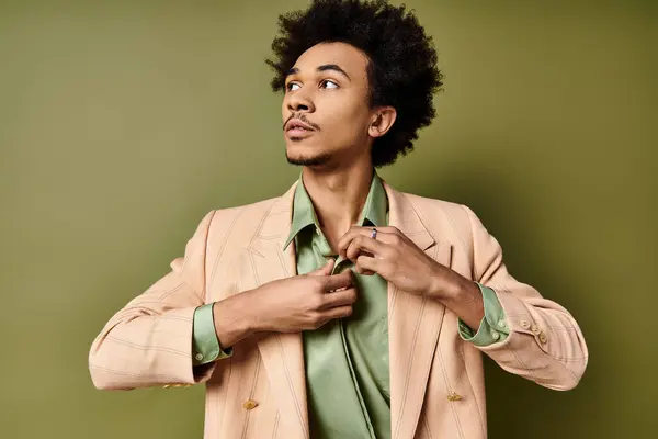 Un hombre afroamericano joven con estilo en un traje es hábilmente abotonar camisa delante de un fondo verde. - foto de stock