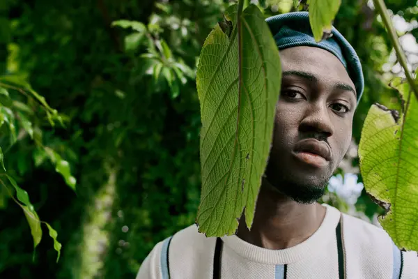 A handsome African American man in a hat stands elegantly posing in lush green garden. — Stock Photo