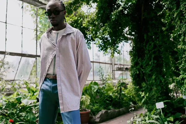 Handsome African American man poses stylishly in front of vibrant green house. — Stock Photo