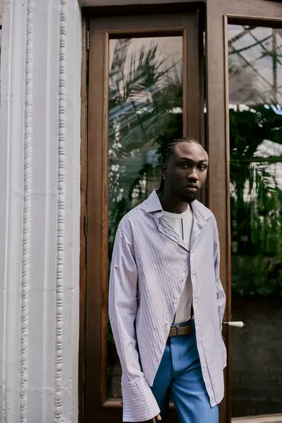 Красивый афро-американец в красивом стиле уверенно стоит перед дверью в ярко-зеленом саду. — стоковое фото