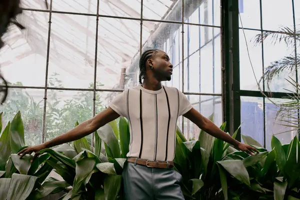 A sophisticated African American man stands elegantly among vibrant green plants in a greenhouse. — Stock Photo