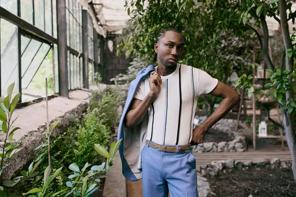 Bello uomo afroamericano in sofisticato stile elegante, indossa una camicia bianca e pantaloni blu, in posa in un vivido giardino verde. — Foto stock