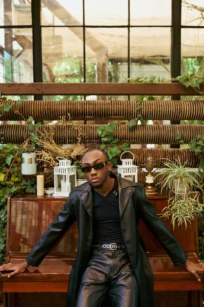 Handsome African American man with dapper style sitting on top of a piano in a vivid green garden. — Stock Photo