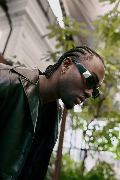 Ein gutaussehender afroamerikanischer Mann posiert in einem lebhaften grünen Garten mit Sonnenbrille und Lederjacke. — Stock Photo