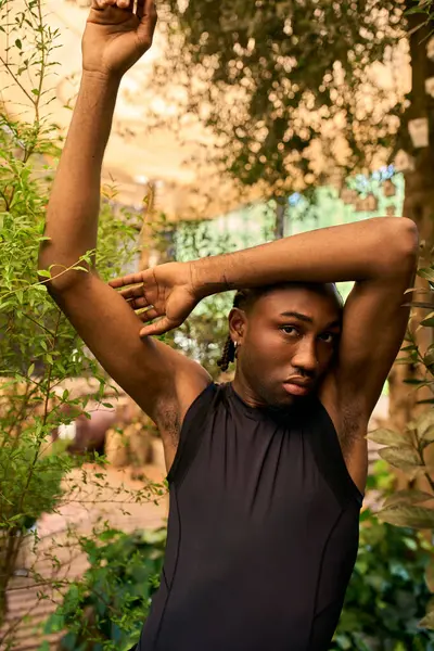 Sophisticated African American man with dapper style raising his arms in green garden. — Stock Photo