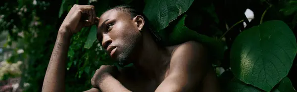A shirtless African American man with dapper style in a lush green garden. — Stock Photo