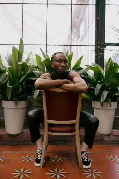 Handsome African American man, sophisticatedly styled, sits crossed-arm in lush green garden. — Stock Photo