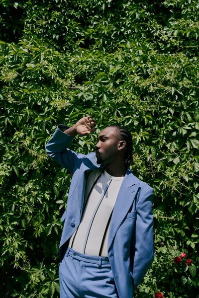Stylish African American man in a blue suit standing elegantly in front of a lush green bush. — Stock Photo