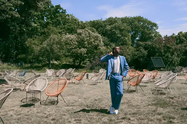 Handsome man in blue suit standing amidst a sea of chairs. — Stock Photo
