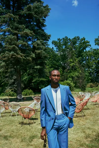 Um homem americano africano sofisticado em um terno azul elegante posa graciosamente em um campo verde exuberante. — Fotografia de Stock