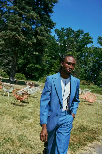 Stylish African American man in blue suit standing in vibrant green place. — Stock Photo