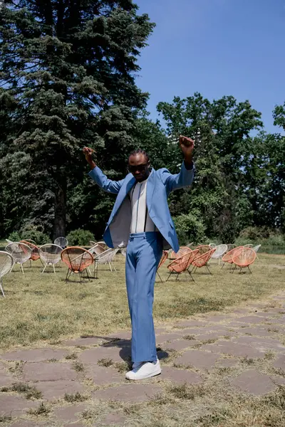 Bonito homem afro-americano em um terno azul posa em meio ao exuberante jardim verde. — Fotografia de Stock