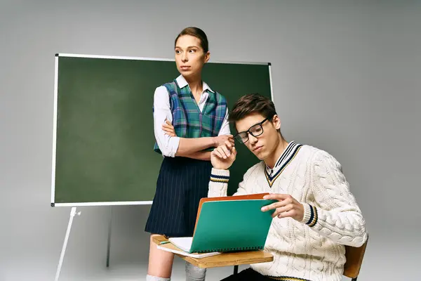 A handsome man and a beautiful woman sitting in front of a green board in a college setting. — Stock Photo