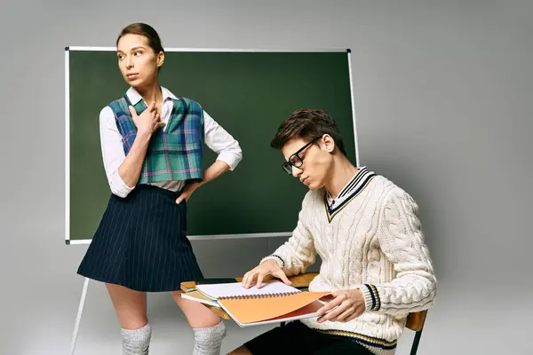 Um homem e uma mulher elegantes sentados junto a um quadro verde em um ambiente universitário. — Fotografia de Stock