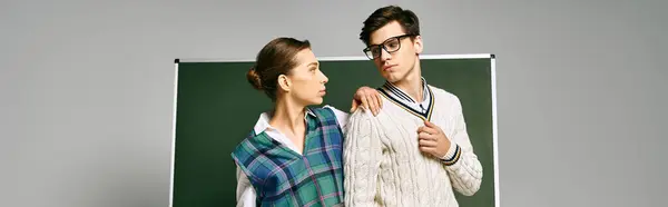 A stylish man and woman standing by a green board in a college setting. — Stock Photo