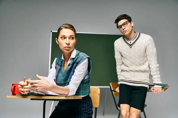 Elegant man and woman in a college setting, seated at a desk in front of a green board. — Stock Photo