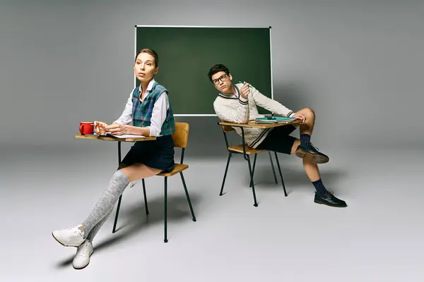 Two stylish students engaged in study at a desk before a green board. — Stock Photo