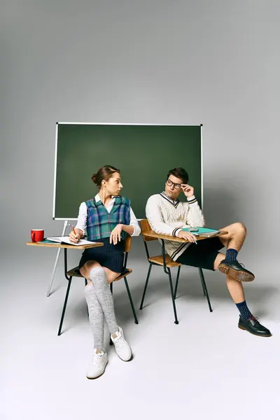 Elegant man and woman seated by a green board in a college setting. — Stock Photo