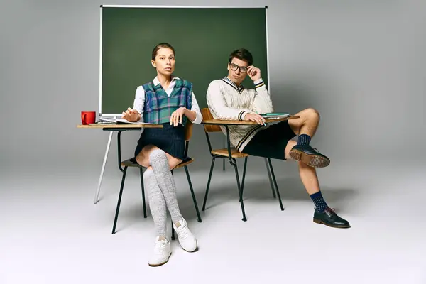 Jeune homme et jeune femme discutant d'idées assis à un bureau devant un tableau vert. — Photo de stock