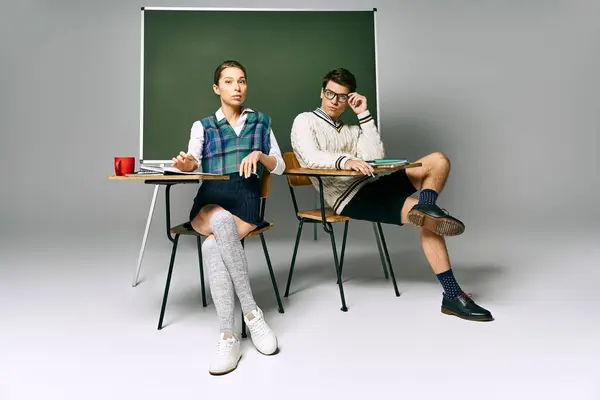 Young man and woman discussing ideas while seated at a desk in front of a green board. — Stock Photo