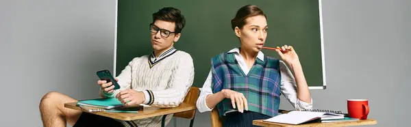 Two students, a male and a female, sitting at a desk in front of a chalkboard in a college setting. — Stock Photo