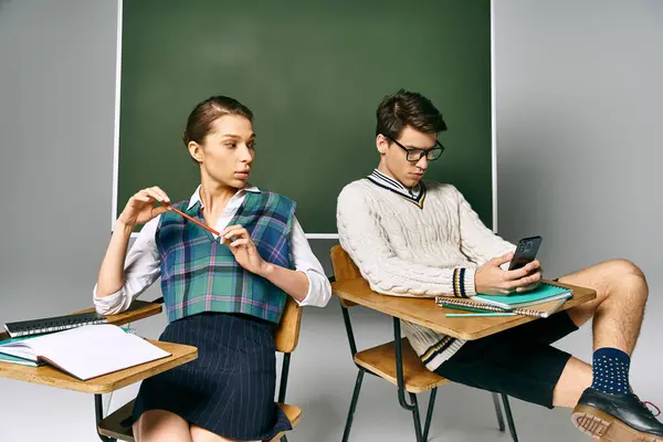 Elegant man and woman sitting in front of green chalkboard, engaged in learning. — Stock Photo