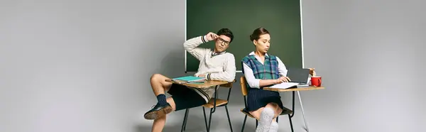 Deux étudiants, un homme et une femme, assis à un bureau devant un tableau vert dans une salle de classe d'université. — Photo de stock