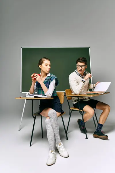 Man and woman sitting at desk, studying in front of green board. — Stock Photo