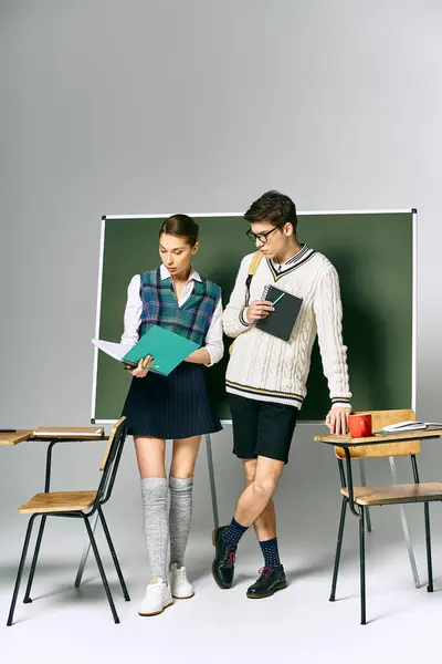Un homme et une femme élégants se tiennent devant un tableau vert dans un cadre universitaire. — Photo de stock