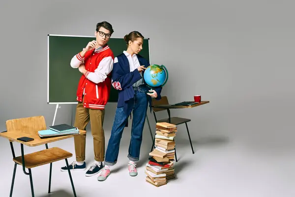 Two students standing at a desk, surrounded by books and a globe. — Stock Photo