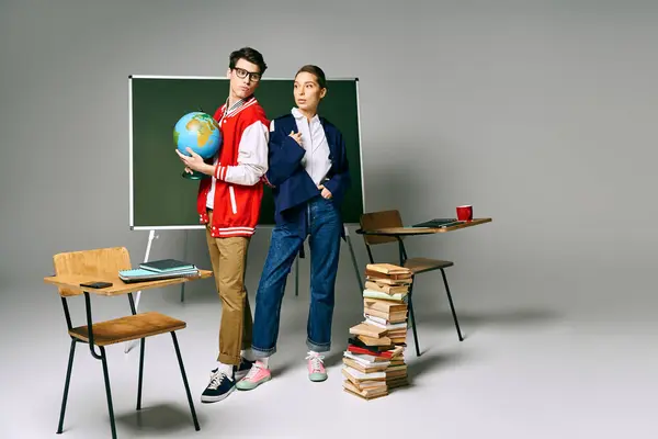 Dos estudiantes posando frente a un tablero verde con un globo terráqueo en un aula universitaria. - foto de stock