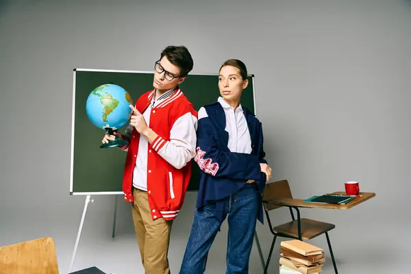 Due studenti tengono un globo, in piedi davanti a una scrivania in una classe. — Foto stock