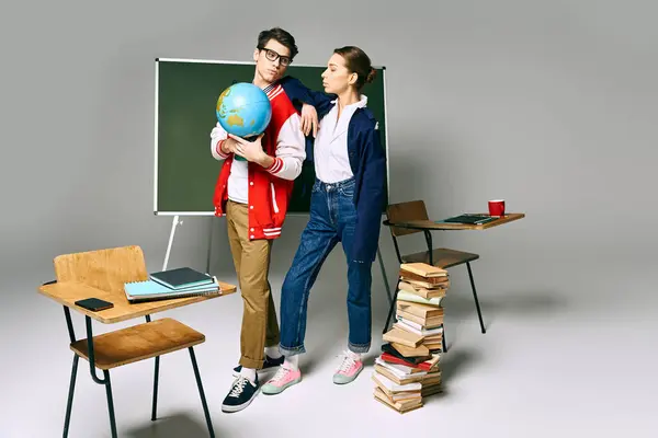 Dos estudiantes universitarios sosteniendo un globo en frente de un tablero verde. - foto de stock