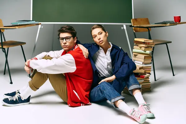 Two young people, a man and a woman, seated on the floor next to a school desk in a college classroom. — Stock Photo