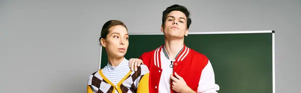Two students, a man and a woman, dressed casually, standing together in front of a green board in a college classroom. — Stock Photo