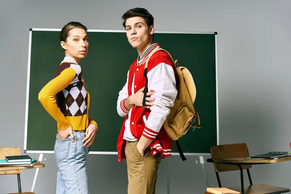 Eine Schülerin und ein Schüler in Freizeitkleidung stehen selbstbewusst vor einer grünen Tafel in einem Klassenzimmer. — Stockfoto