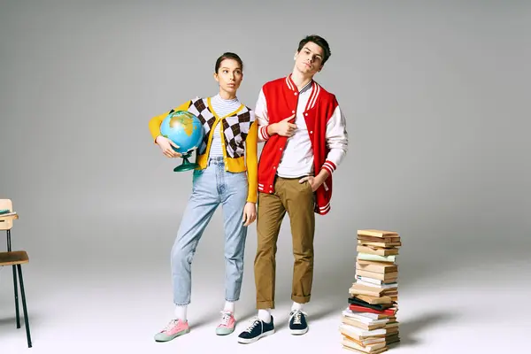 Deux jeunes étudiants posant devant une grande pile de livres dans un cadre de classe. — Photo de stock