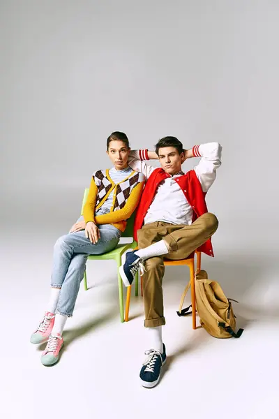 Two young people, a man and a woman, sitting on colorful chairs in a college classroom. — Stock Photo