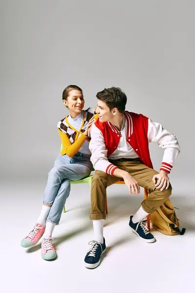 A male and female students in relaxed college attire contemplatively sit together on a chair. — Stock Photo