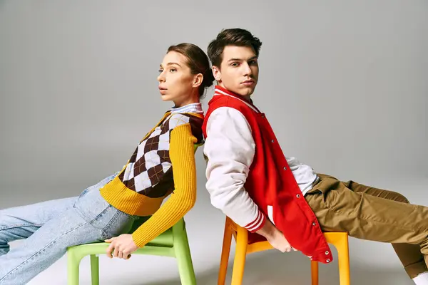 Two young people, male and female students, sitting on colorful chairs in a vibrant classroom. — Stock Photo