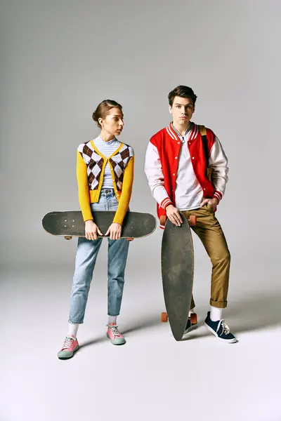 Two stylish young adults hold skateboards in front of a white backdrop. — Stock Photo