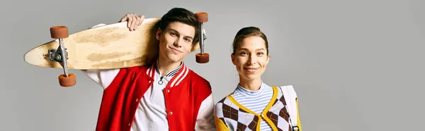 Two stylish individuals holding a skateboard against a gray backdrop. — Stock Photo