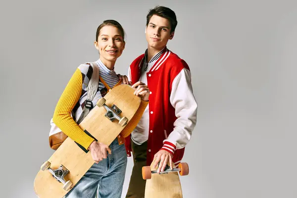 Due giovani con fiducia tengono skateboard su uno sfondo grigio. — Foto stock