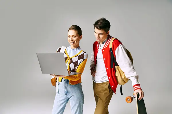 Jóvenes estudiantes masculinos y femeninos sosteniendo portátil y monopatín en el entorno de la universidad. — Stock Photo