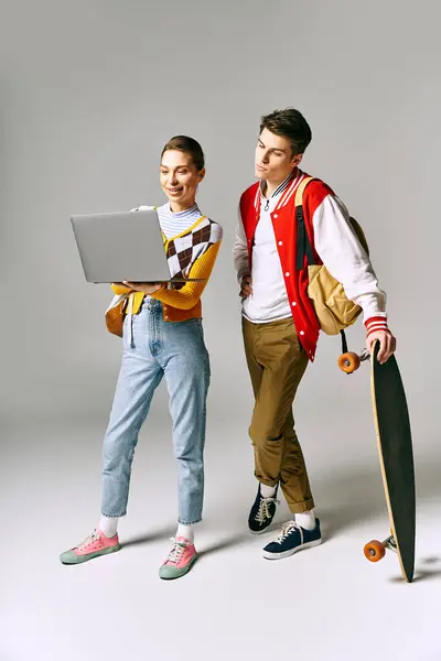Dois jovens seguram um laptop e skate em um ambiente de sala de aula. — Fotografia de Stock