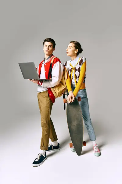 Young male and female students hold laptop and skateboard. — Stock Photo