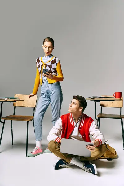Un jeune homme et une jeune femme étudiants assis sur le sol, collaborant sur un ordinateur portable. — Photo de stock