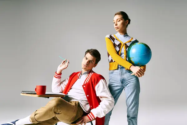 A male and female students sit holding a globe, deep in thought and wonder. — Stock Photo